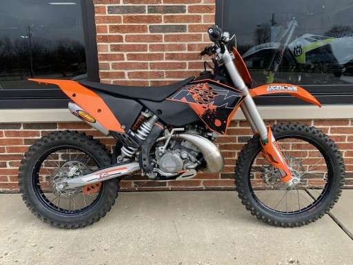 an orange and black dirt bike parked in front of a brick building next to a window