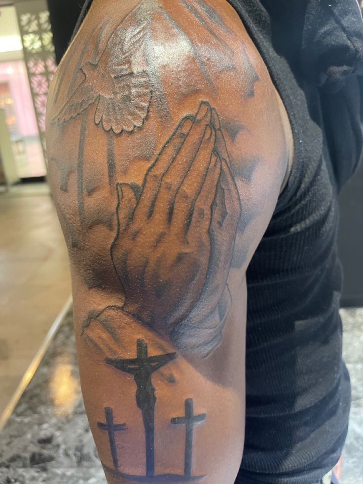 a man with a cross and praying hands tattoo on his arm