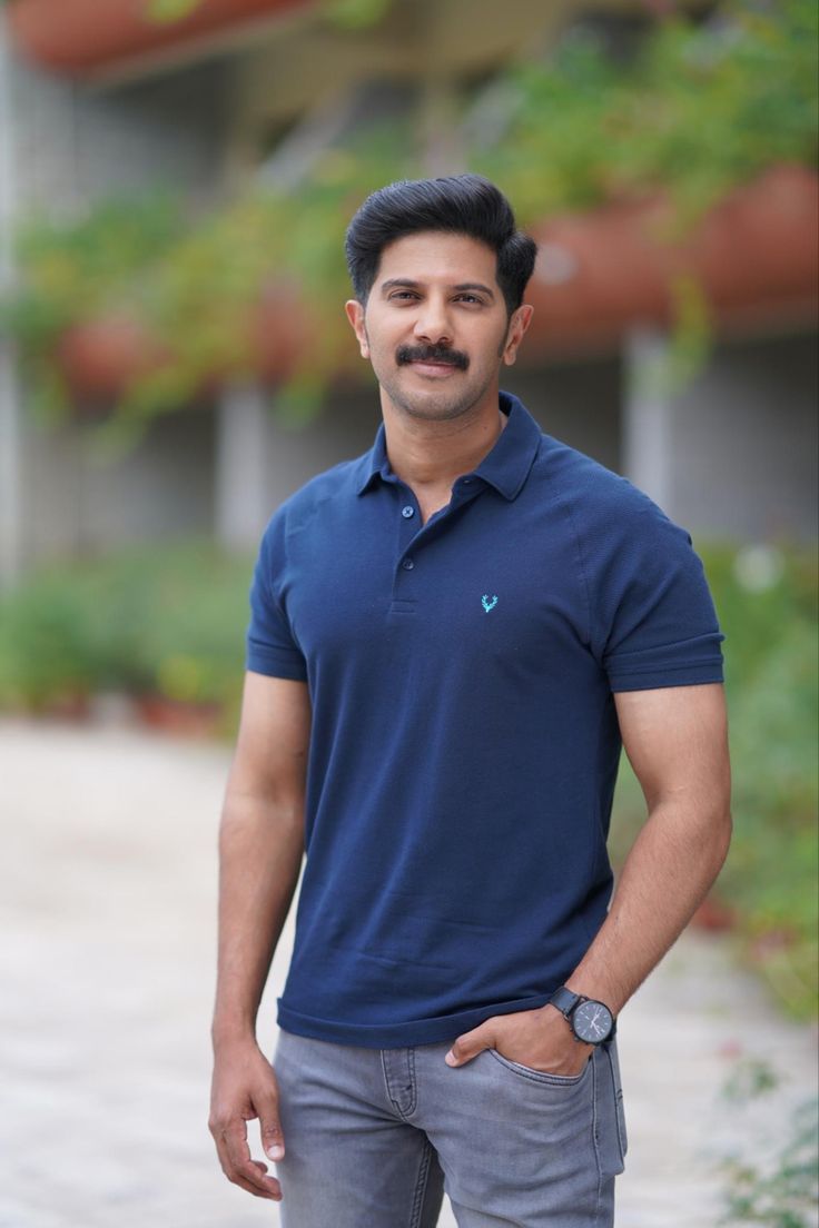 a man standing in front of a building wearing a blue shirt and grey pants with his hands on his hips