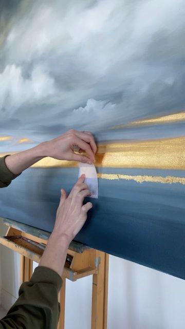 a person is painting on a canvas with clouds in the sky behind them and one hand reaching out to touch it