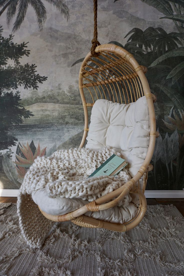 a wicker hanging chair with a book on it in front of a wall mural