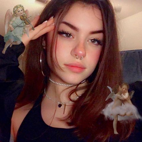 a girl with piercings on her nose and an angel figurine behind her