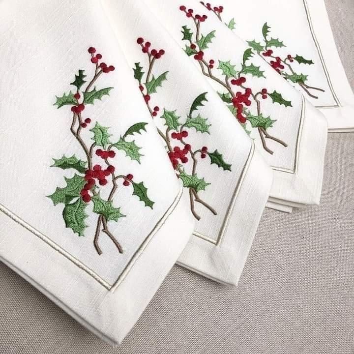 four white christmas napkins with holly and berries on them