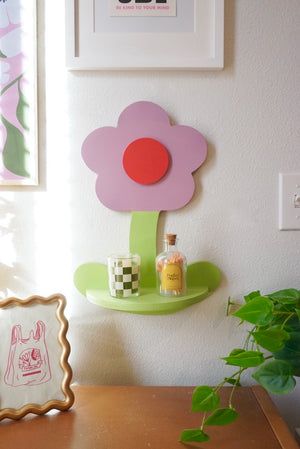 a wooden table topped with a green shelf next to a potted plant and pictures on the wall