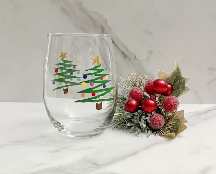 a wine glass with a christmas tree painted on the side next to a holiday decoration