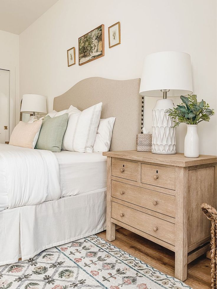 a bed with white sheets and pillows in a bedroom next to a lamp on a dresser