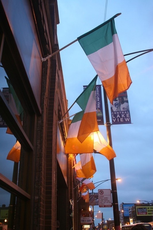 flags hanging from the side of a building on a city street at dusk with people walking by