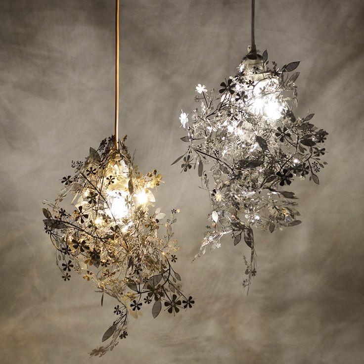 two chandeliers hanging from the ceiling with flowers and leaves on them, one light is