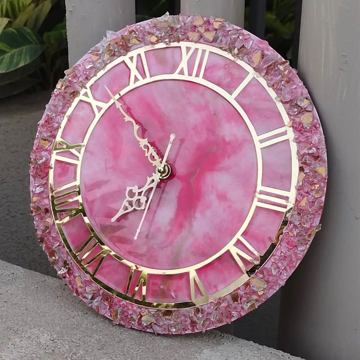 a pink and gold clock with roman numerals on it's face is shown