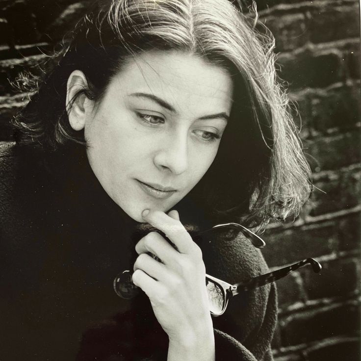 a black and white photo of a woman leaning against a brick wall holding a pipe