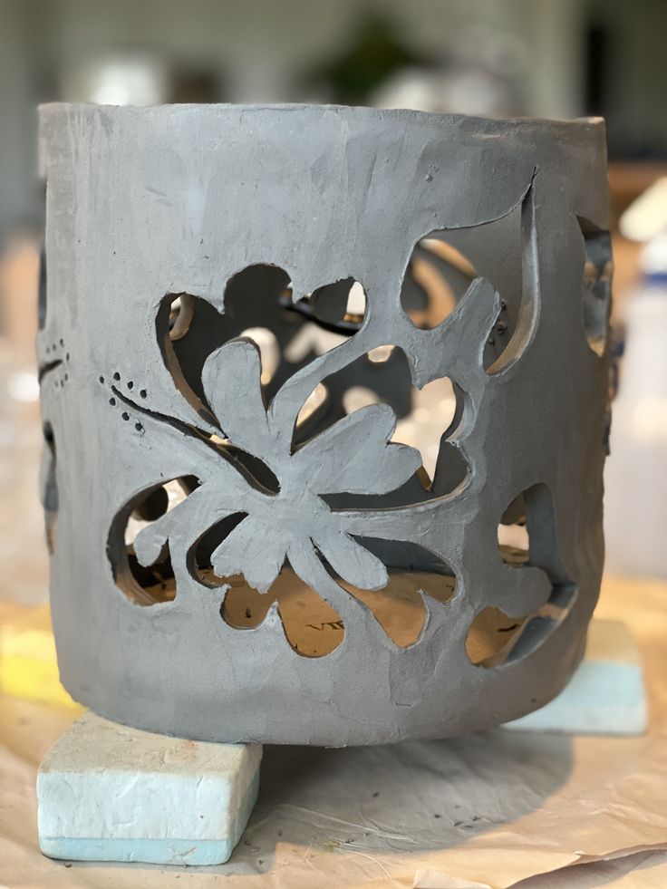 a gray vase sitting on top of a table next to a block of wood and paper