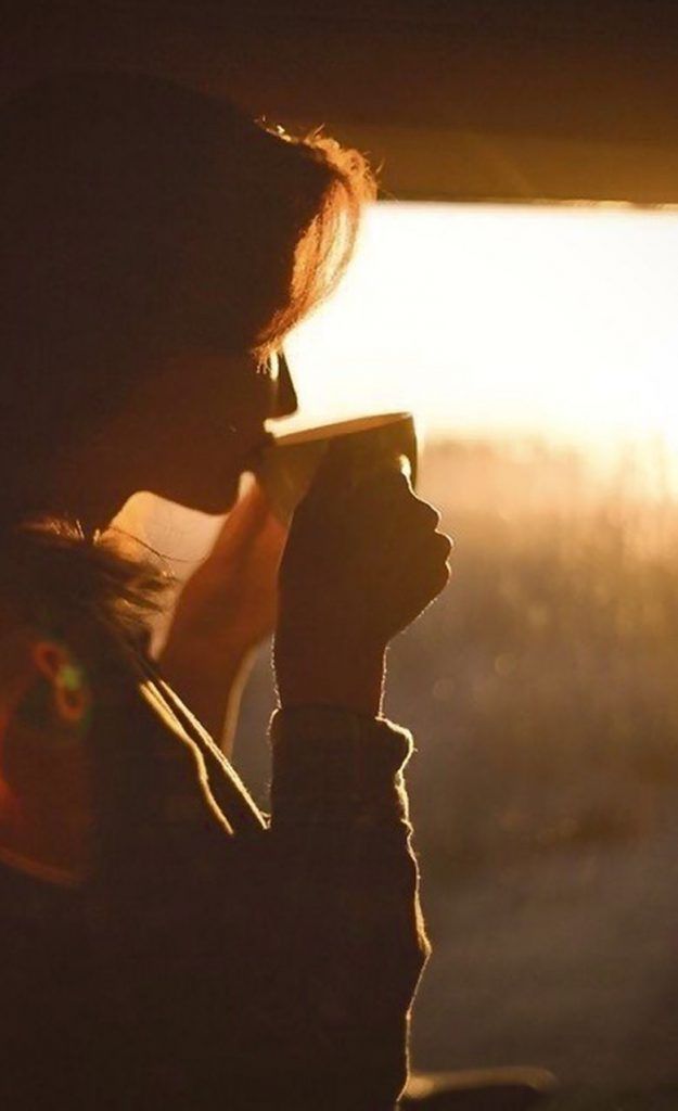 a woman is drinking from a cup in the sunlit room with her hand up to her face