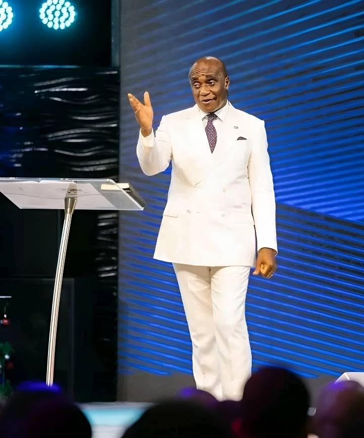 a man in a white suit standing at a podium with his hand up to the side