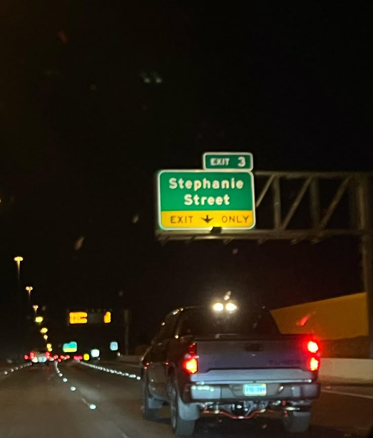 two cars are driving down the highway at night with traffic lights on and street signs above them