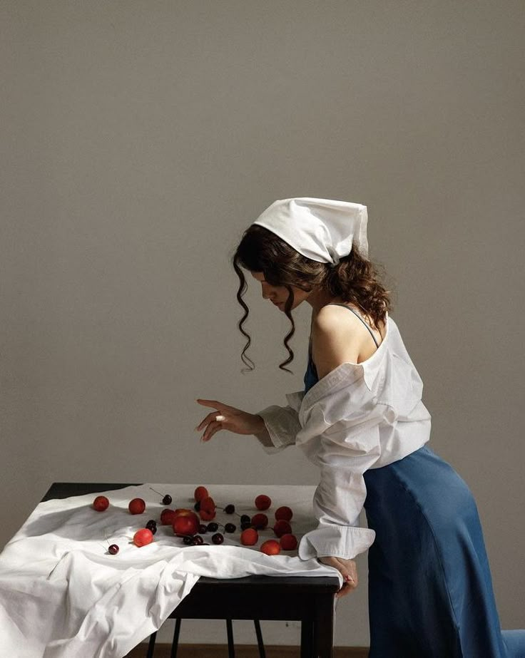 a woman in a white shirt and blue skirt standing over a table with strawberries on it