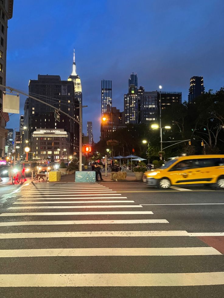 a city street at night with cars and people crossing the street in front of tall buildings