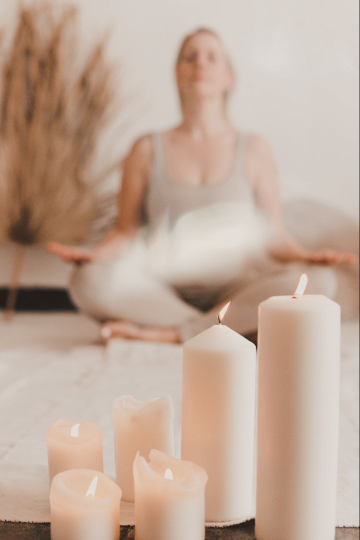 a woman is sitting on the floor in front of candles and an open yoga mat