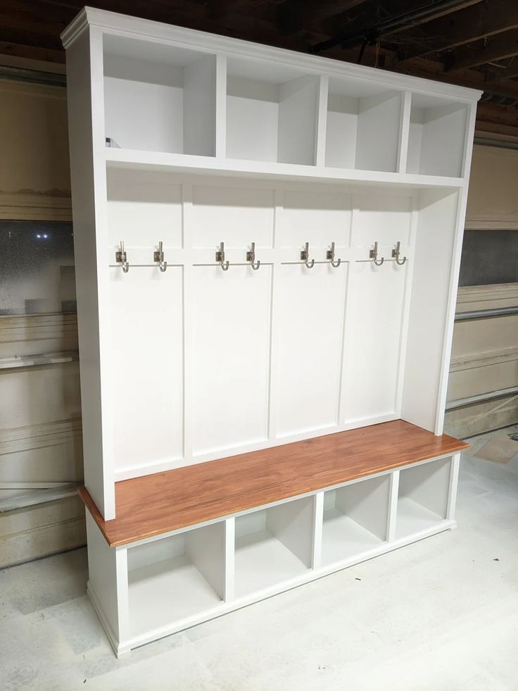 an empty white bench with wooden seat and storage units on the wall behind it in a garage