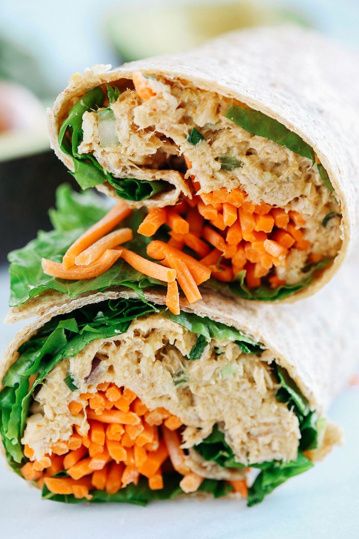 two wraps with carrots, lettuce and meat in them are stacked on top of each other