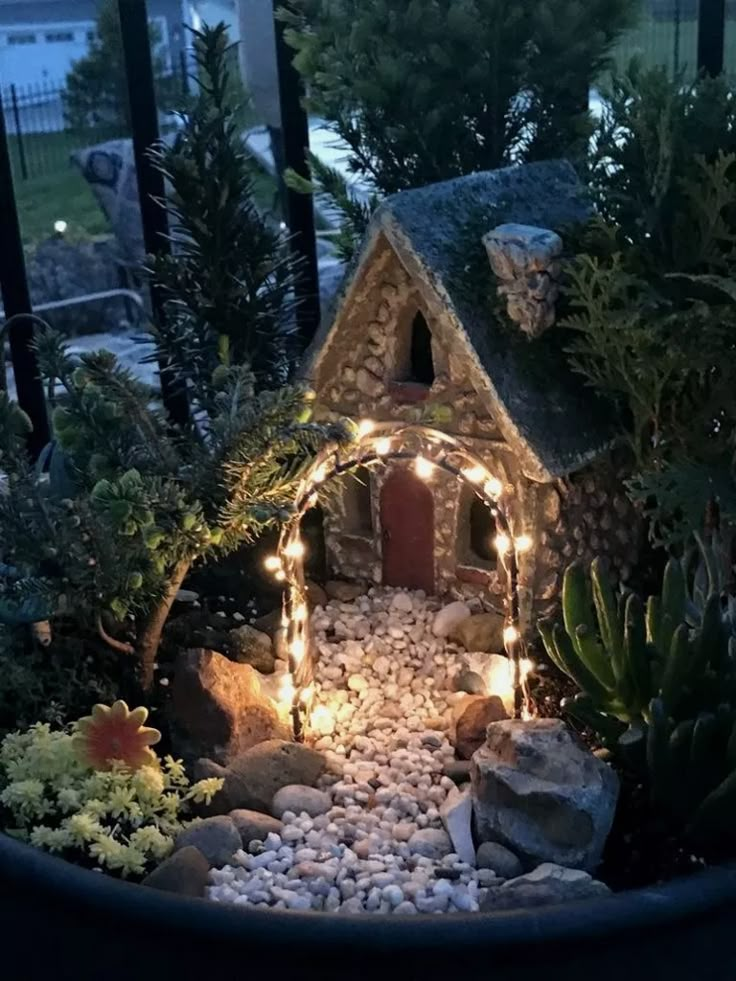 a small garden with rocks and plants around it, lit up by fairy lights in the middle