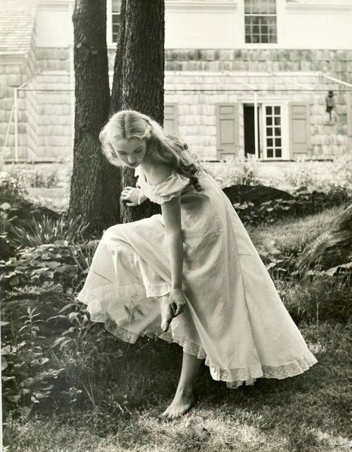 an old black and white photo of a woman in a dress leaning against a tree