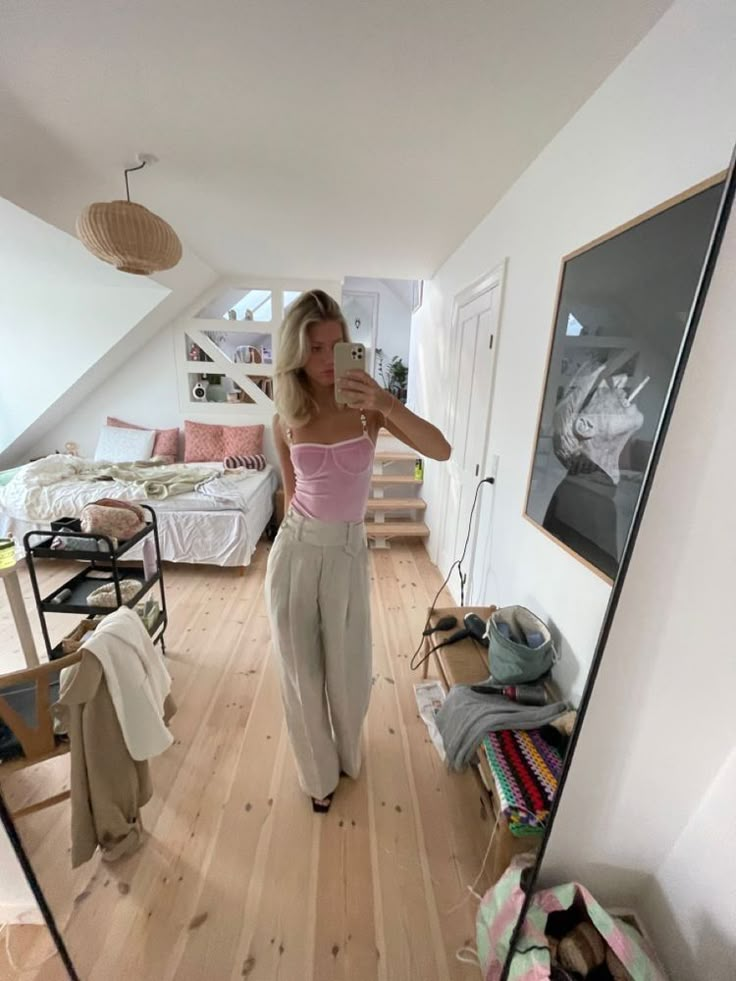 a woman taking a selfie in the mirror while standing on a hardwood floor next to a bed