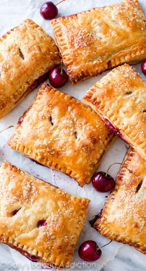 cherry hand pies on parchment paper with fresh cherries