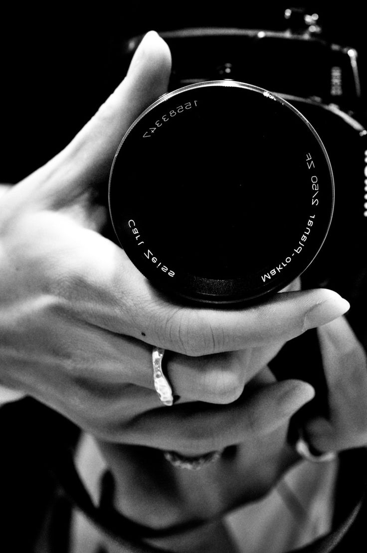 black and white photograph of person holding camera in their hands with the lens pointed up