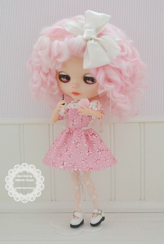 a doll with pink hair is holding a cupcake in her hand and standing next to a wall