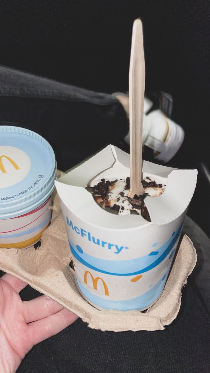 a person holding a paper container with food in it and a spoon sticking out of it