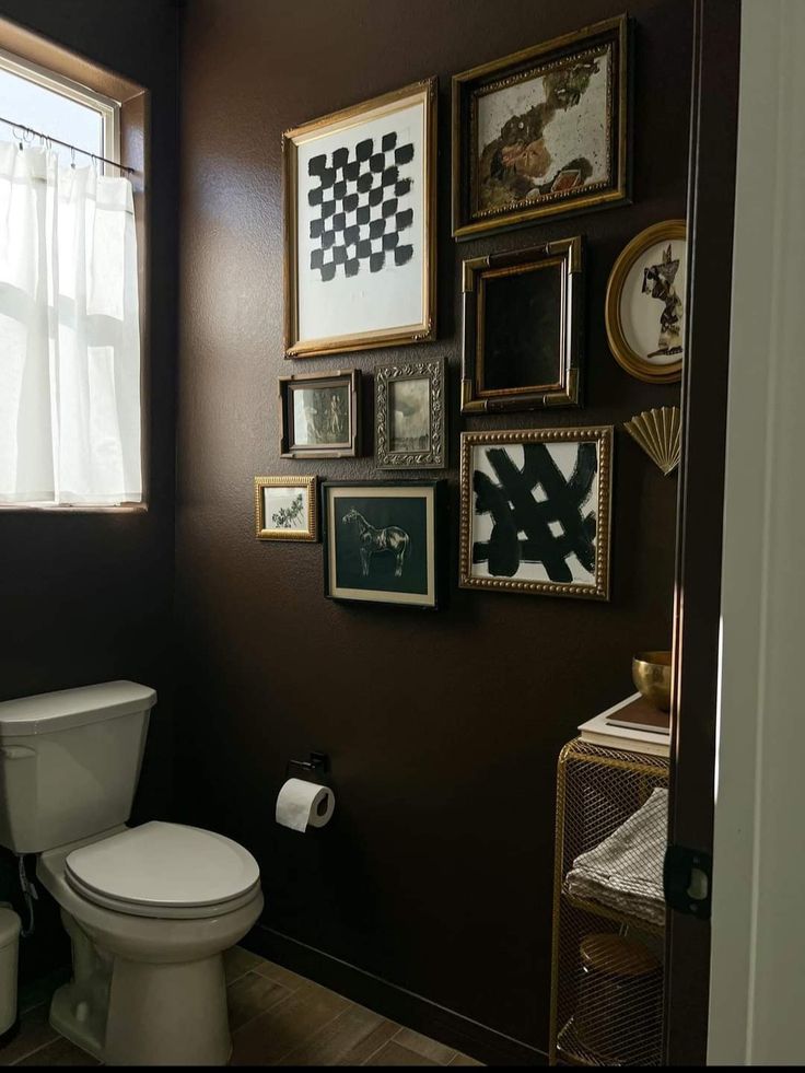 a white toilet sitting in a bathroom next to a wall filled with pictures and framed art