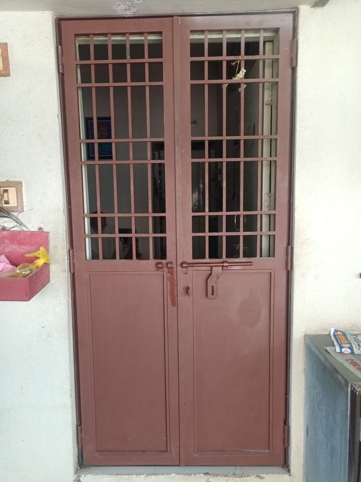 two brown doors are open on the side of a white wall and there is a trash can in front of them