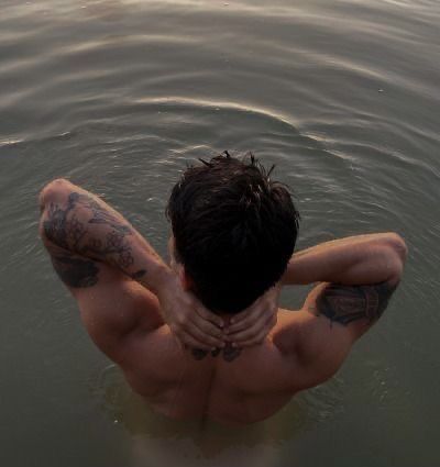 a man in the water with his back turned to the camera and tattoos on his chest