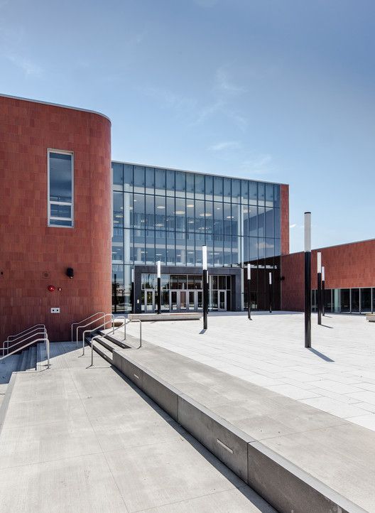 an empty courtyard in front of a building with glass walls and stairs leading up to the entrance