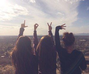 three girls standing on top of a hill with their hands in the air