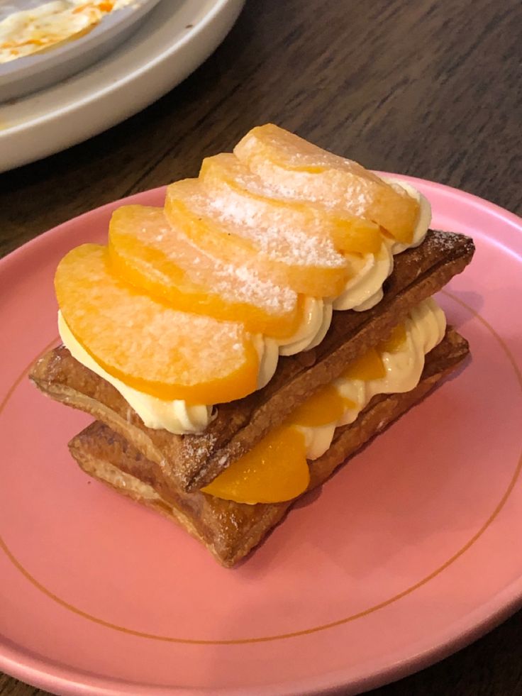 a sandwich with orange slices and cream on it sits on a pink plate next to a fork