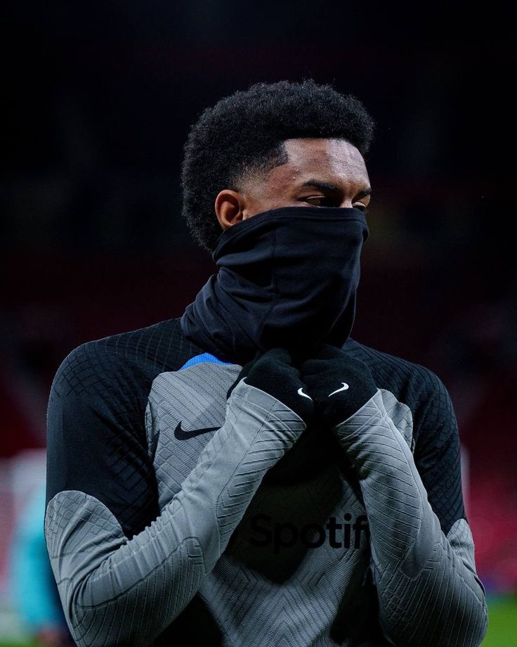 a soccer player wearing a black face mask and holding his hands to his face while standing on the field