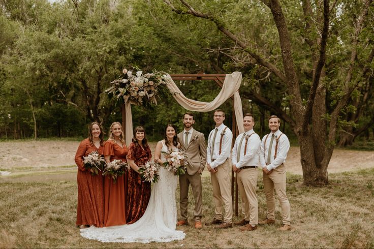 a group of people standing next to each other in front of a wooden arch with flowers on it