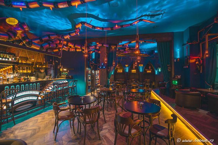 the interior of a bar with many tables and stools in front of colorful lights