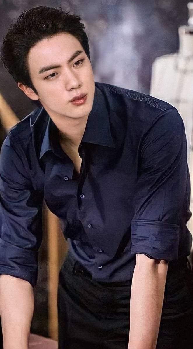 a young man in a blue shirt and black pants leaning on a table next to a white cake