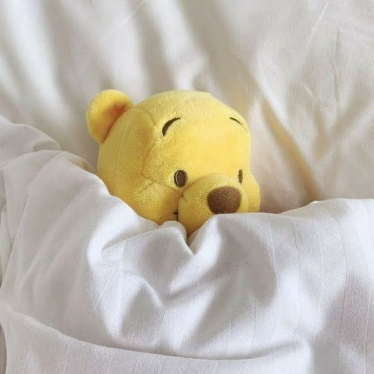 a winnie the pooh stuffed animal laying in bed with white sheets on it's side