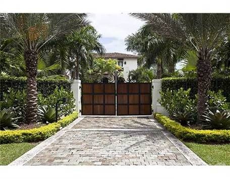 an entrance to a home with palm trees and bushes in front of the gated area