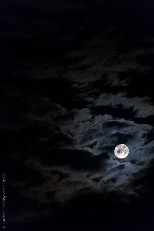 the full moon is shining brightly in the night sky with clouds and dark blue skies