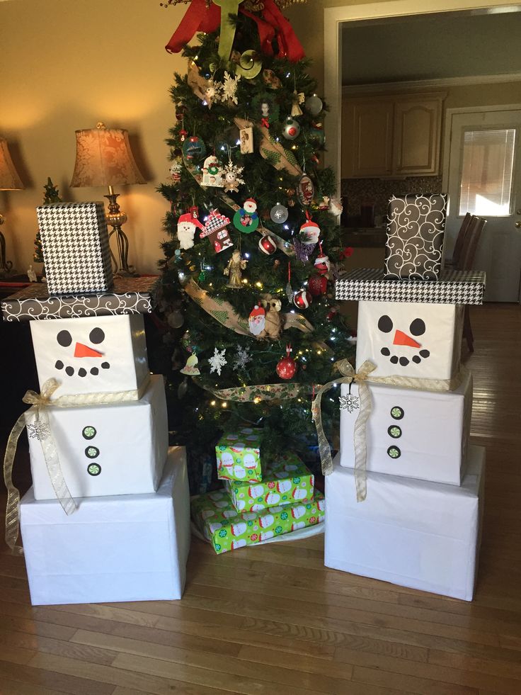 a christmas tree with presents under it in front of two snowmen on the ground