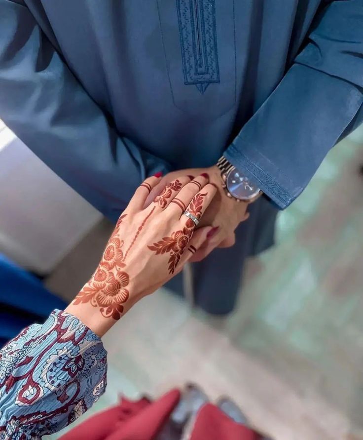 two people holding hands with hendi tattoos on their wrists and arms, both wearing blue shirts