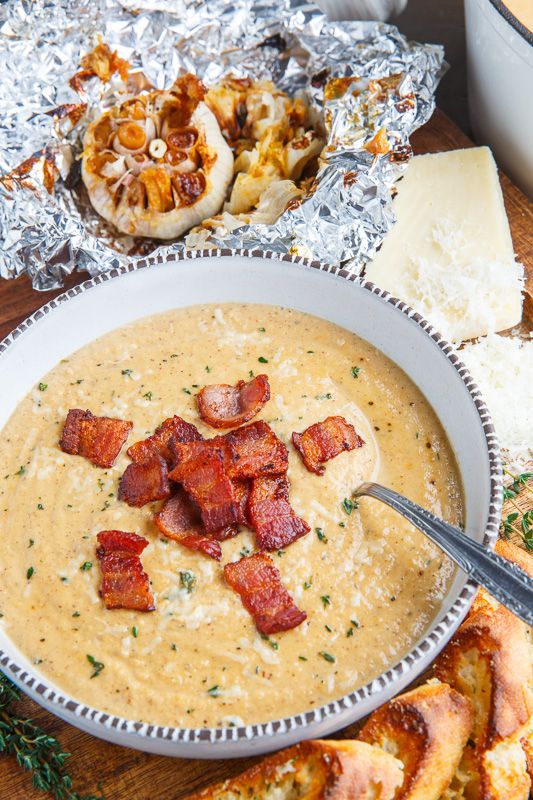 a bowl of soup with bacon and cheese on the side next to some bread slices