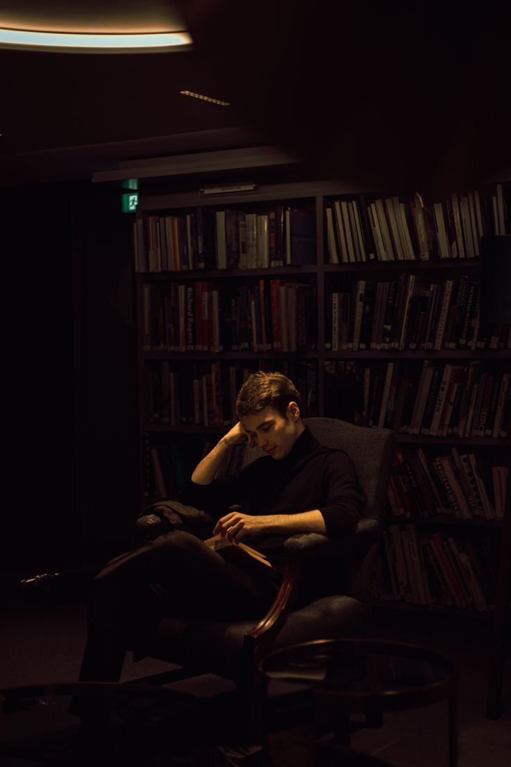 a man sitting in a chair with his hand on his face while reading a book