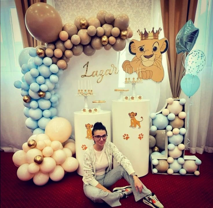 a man sitting on the floor in front of balloons and decorations for a lion themed birthday party