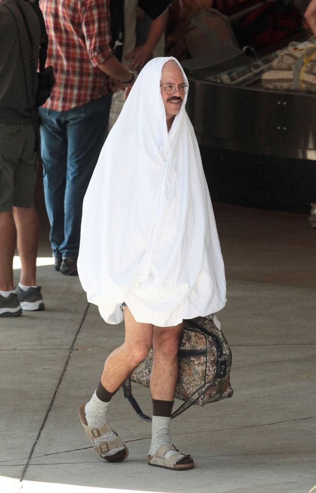 a man in a towel is walking down the street with his foot on a backpack