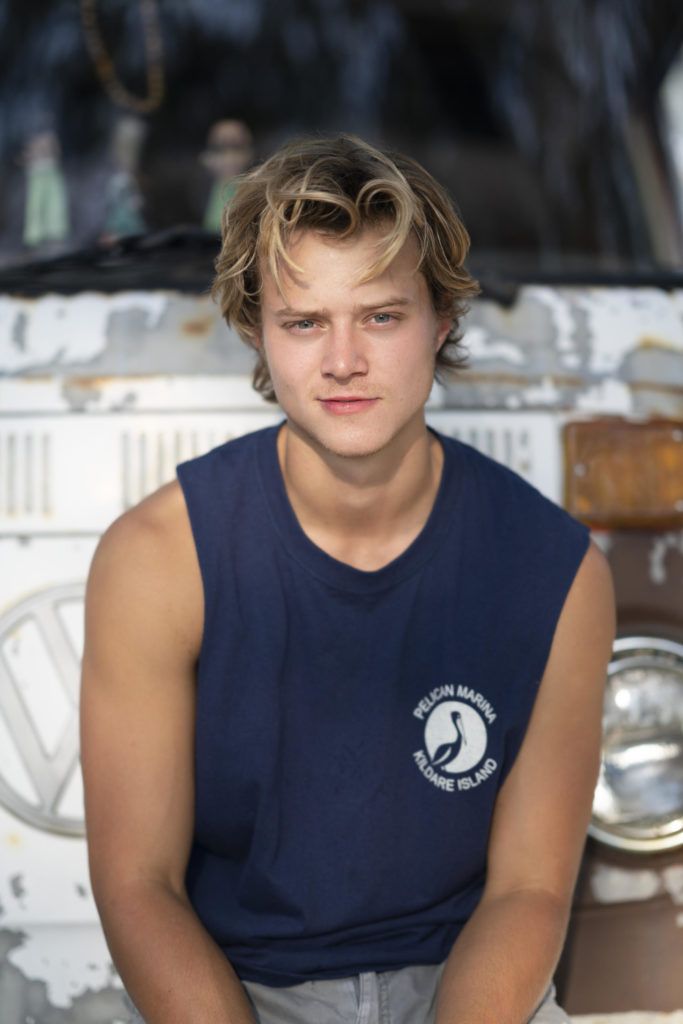 a young man sitting in front of an old van with his hands on the ground